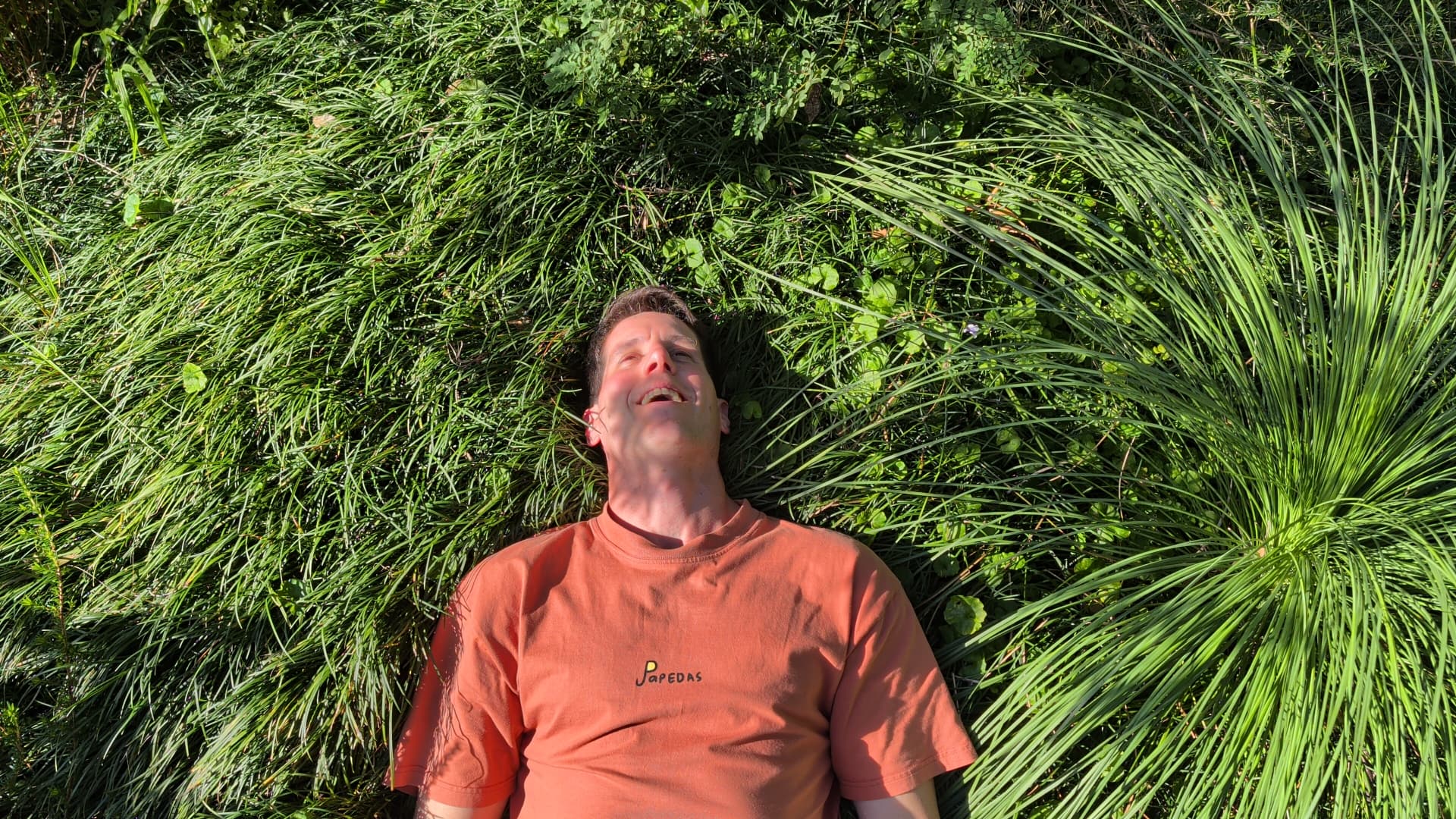 Sean Vitorovic lying back in long grass, laughing in the sun